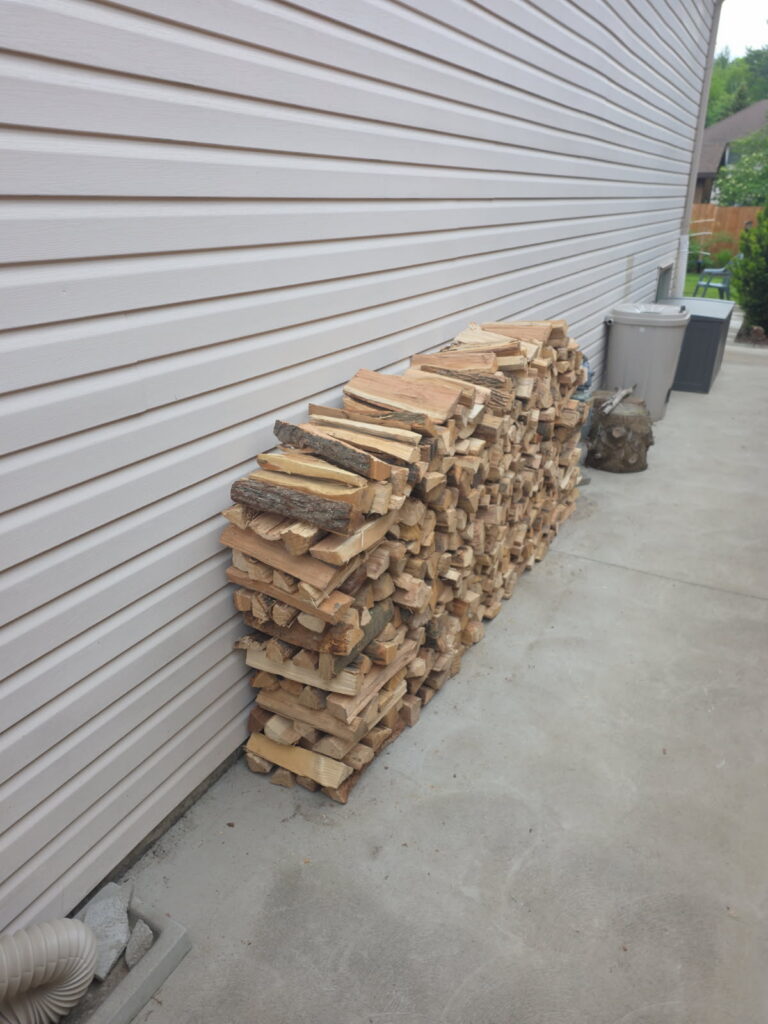 a row of stacked firewood next to a house